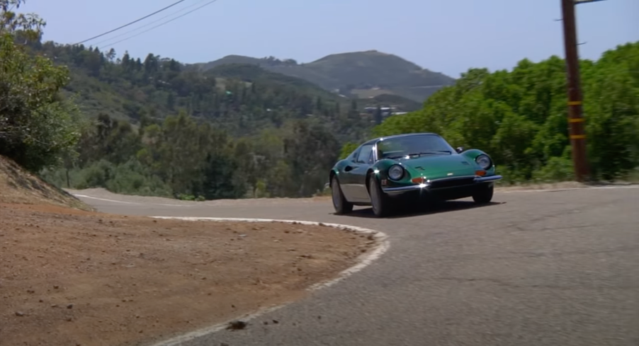 Green 1974 Ferrari Dino driving around a corner on a road.