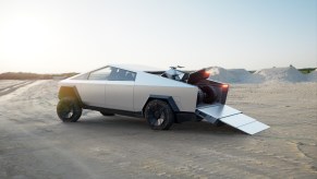 A Tesla Cybertruck carrying a "cyber quad" 4WD with its tailgate and a ramp down.