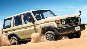 Tan toyota Land Cruiser SUV driving through the desert, blue sky visible in the background.