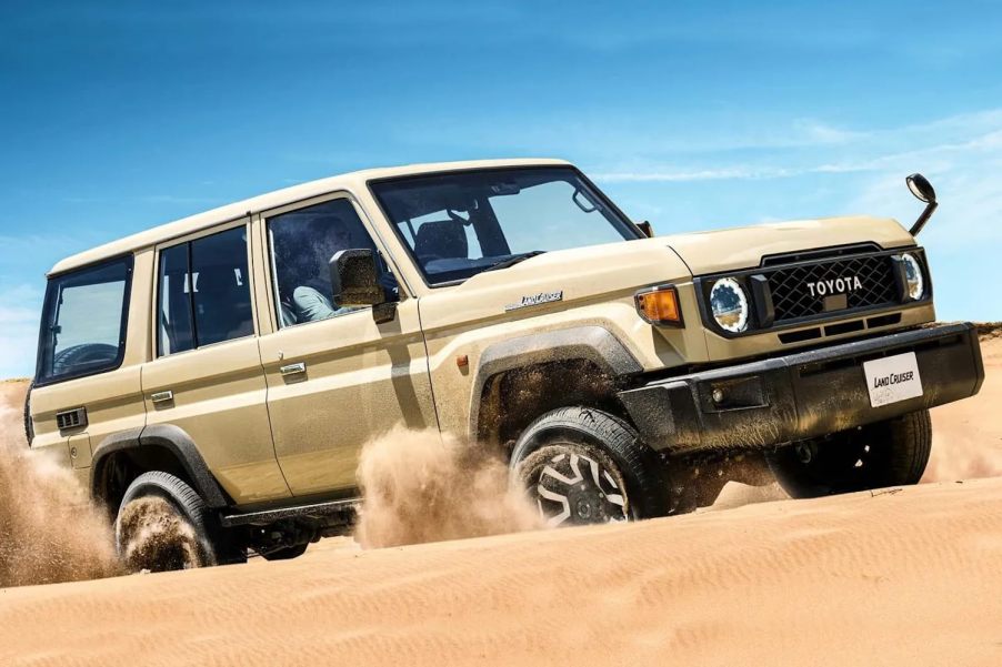 Tan toyota Land Cruiser SUV driving through the desert, blue sky visible in the background.