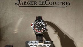 An Aston Martin series watch on display beneath a Jaeger-LeCoultre sign.