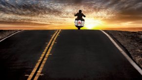 A motorcycle commuter crests a hill on his bike.