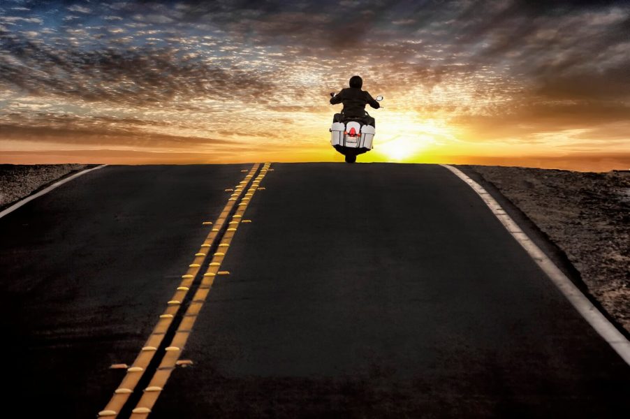 A motorcycle commuter crests a hill on his bike.