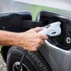 A blue collar worker's hand as they plug an F-150 Lightning electric pickup truck into a Ford Pro charger.