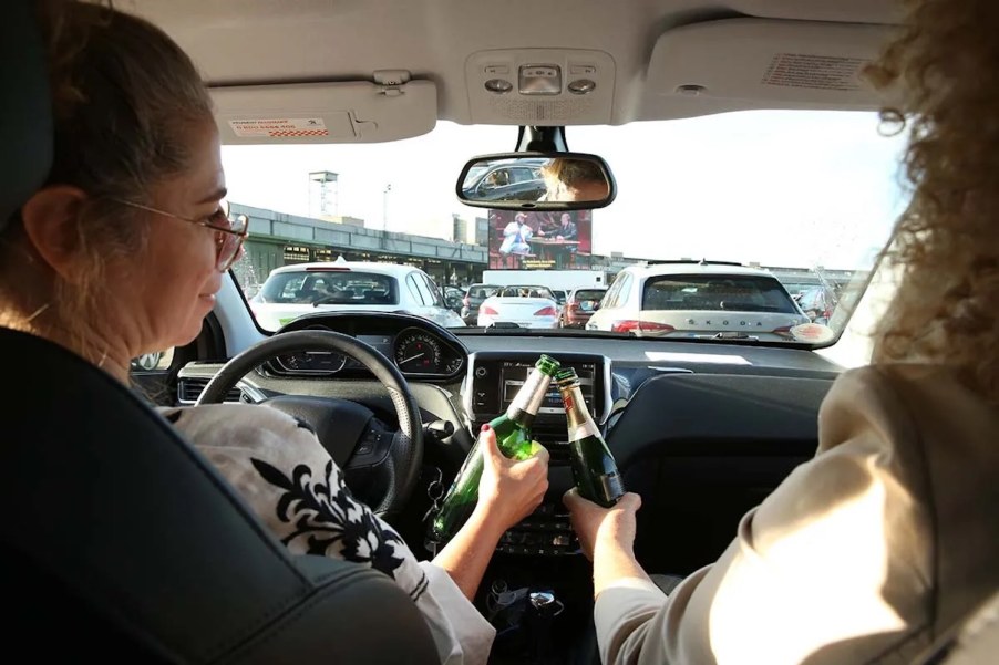 Two drivers cheer with open beers while driving a car.