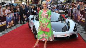 Dame Helen Mirren poses on the red carpet in front of a McLaren supercar during the Hobbs and Shaw Fast and Furious premiere