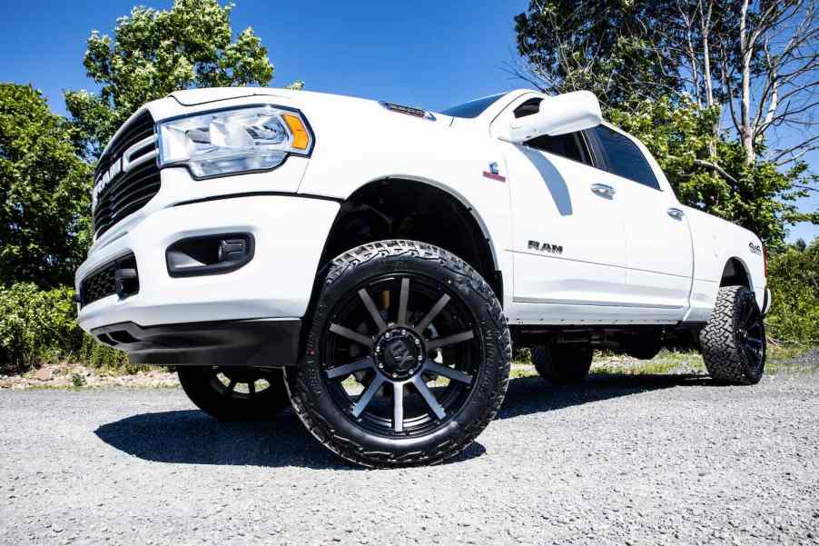 The aftermarket rims under a lifted white Ram pickup truck parked in a lot.