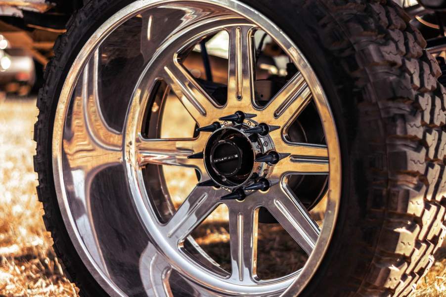 Spiked lug nuts and chrome rim beneath a lifted pickup truck.