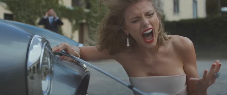 Taylor Swift sings next to a smashed Shelby Cobra sports car.