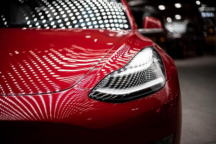 Hood and headlight of a red Tesla Model 3.