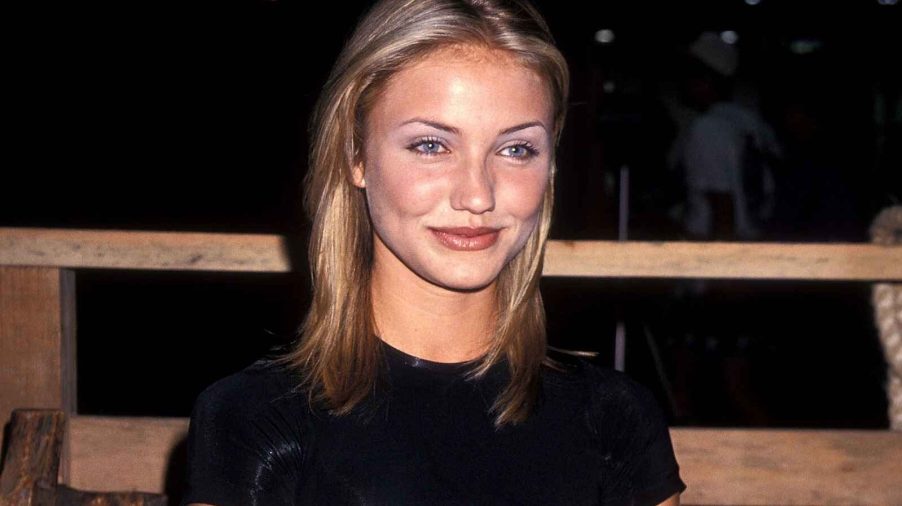 Cameron Diaz sitting on wooden bench in Las Vegas in 1995 wearing a black short sleeve top and blue satin skirt