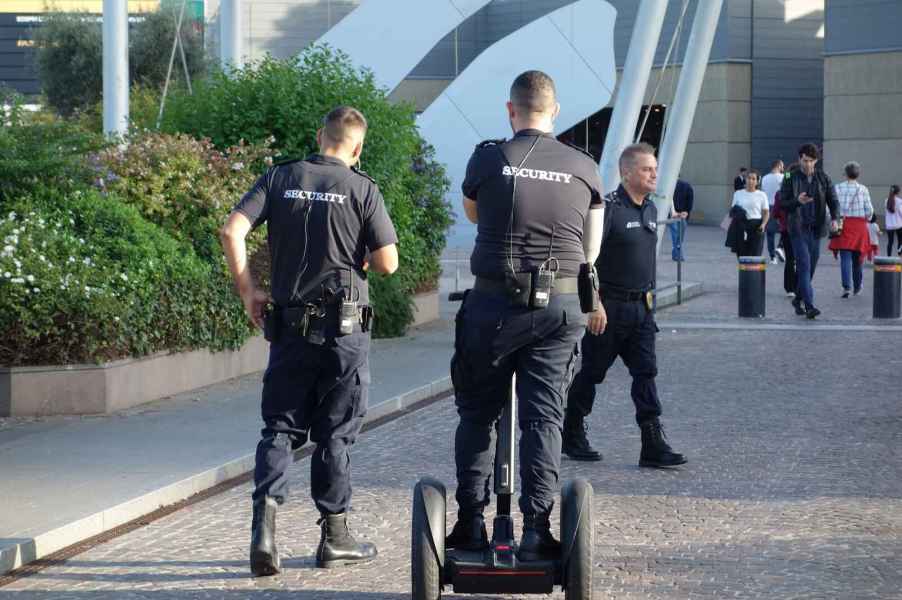 A security guard rides a Segway on a paver stone road with his back turned to the camera