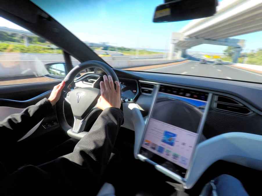 A person's hands are shown driving a Tesla Model X featuring autopilot