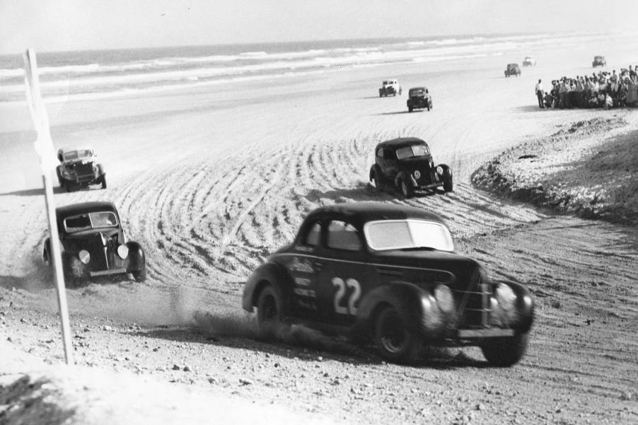 Two door coupe stock cars round the hairpin turn at Daytona Beach during inaugural NASCAR race.