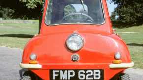 red one-seat micro car parked in front of a grass lawn