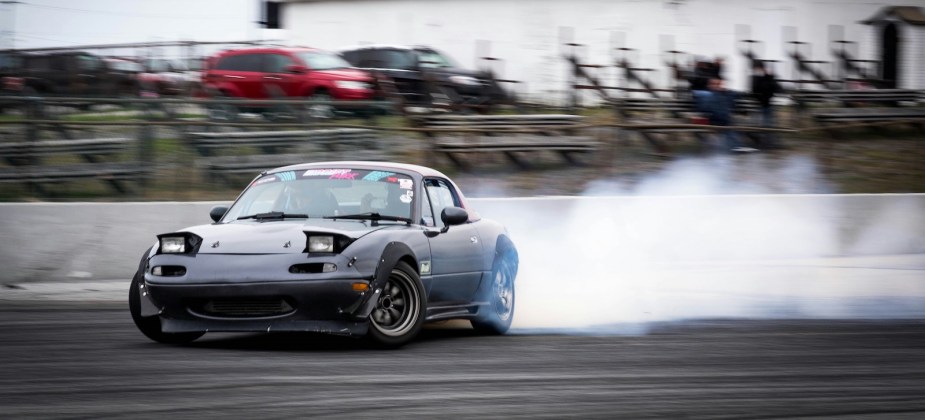 Gray Mazda Miata drift car skidding on a race track.