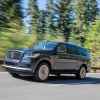 A blue 2022 Lincoln Navigator SUV driving on the read with evergreen trees in the background