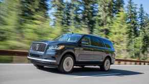 A blue 2022 Lincoln Navigator SUV driving on the read with evergreen trees in the background