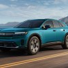 A blue 2024 Honda Prologue EV driving on a high paved road guardrail, sky, and mountain in background