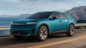 A blue 2024 Honda Prologue EV driving on a high paved road guardrail, sky, and mountain in background