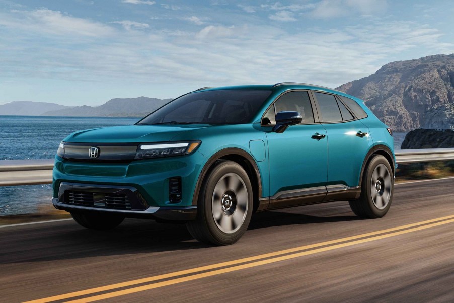 A blue 2024 Honda Prologue EV driving on a high paved road guardrail, sky, and mountain in background