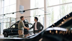 Car salesman shakes a customer's hand in a dealership.