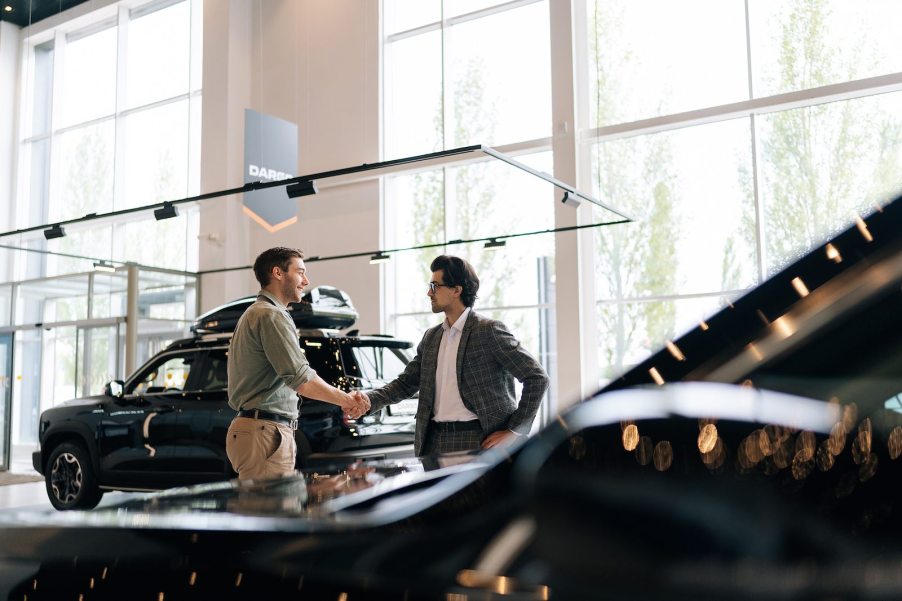 Car salesman shakes a customer's hand in a dealership.