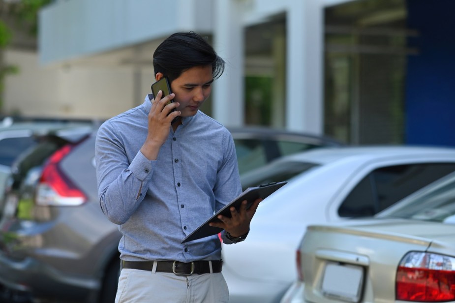 Car salesman reads off a clipboard during a phone call in a dealership.