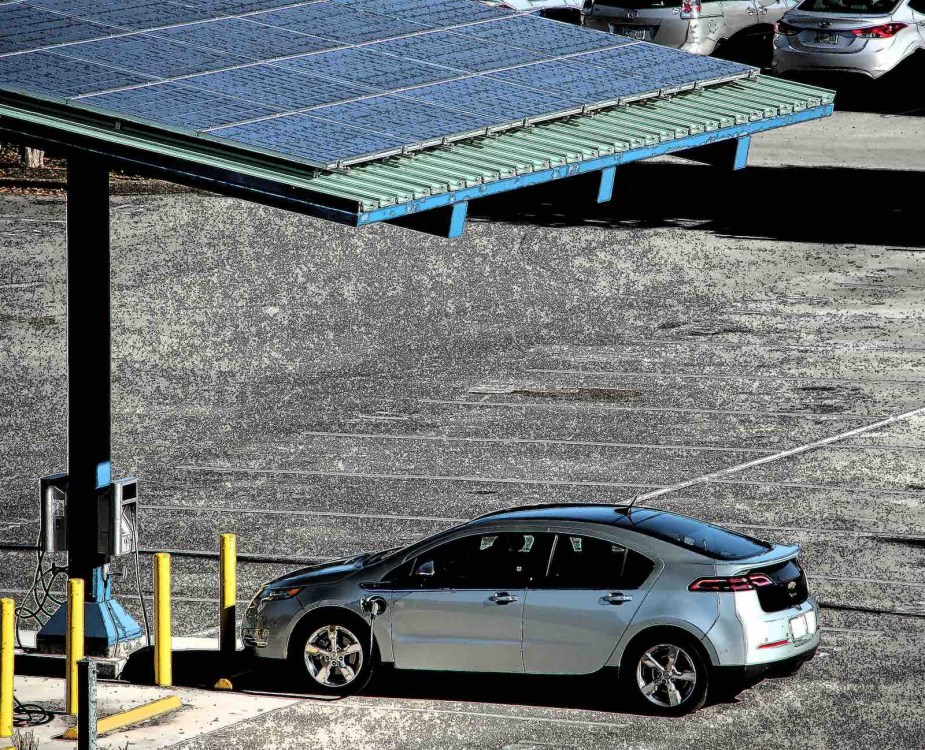 Silver Chevrolet Volt sedan plugged in to a charging station by a solar panel.