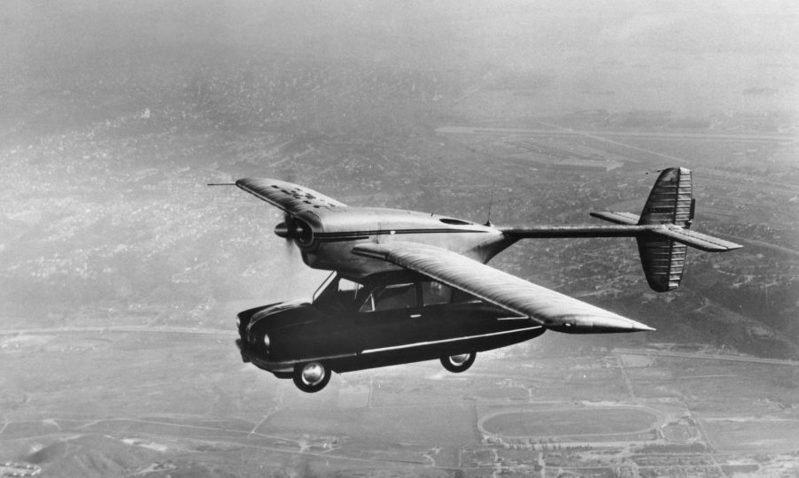 Black and white photo of a flying car with plane wings.