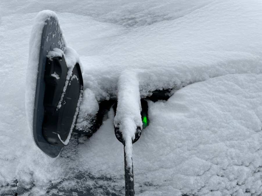 An EV charge port with charger plugged in during a snow storm covered in snow