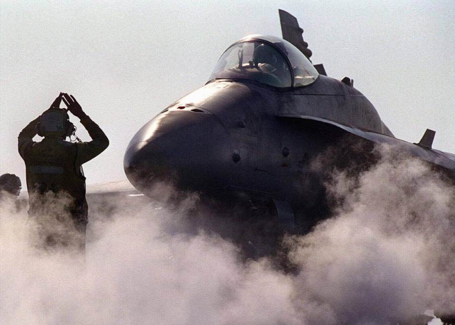 An F-18 preps to take off from an aircraft carrier deck with a steam catapult.