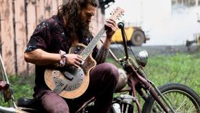 Jason Momoa plays a guitar on a motorcycle.