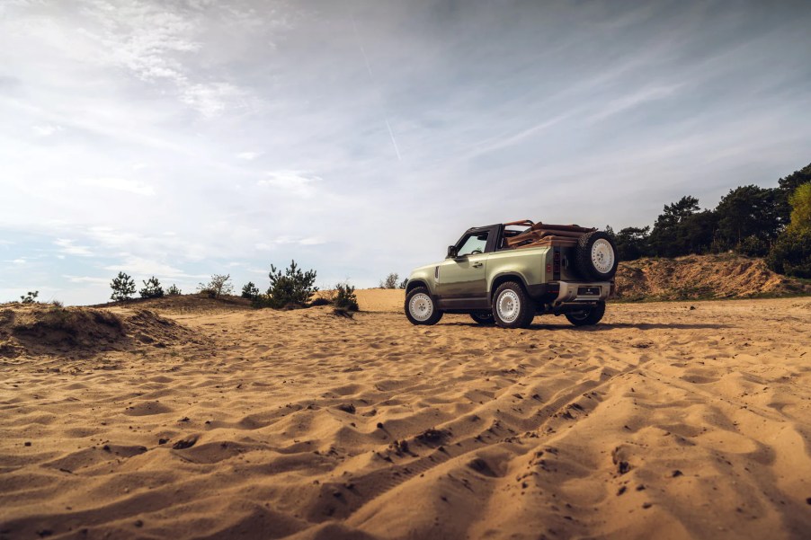 Light green custom Land Rover Defender convertible parked on the sand of a beach.