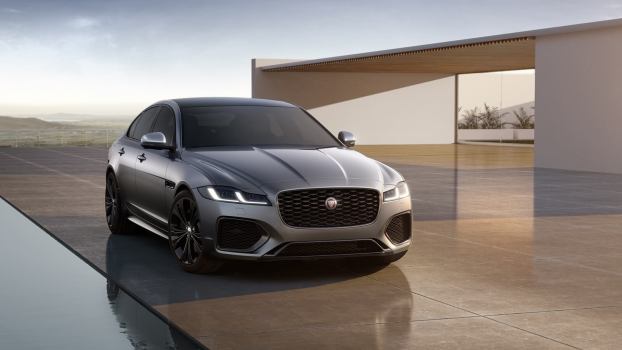 A Jaguar XF, one of the luxury cars with the lowest cost to own, poses next to a home.