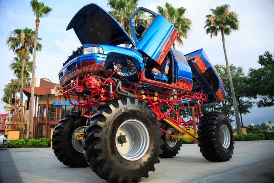 Blue and orange lifted dodge truck parked in front of palm trees.