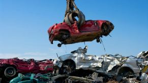 Red sedan picked up by a crane in a salvage yard