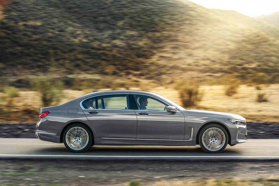 A silver BMW 7 Series luxury car drives on a mountain road.