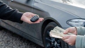 A person offers a stack of paper bills in exchange for car keys.