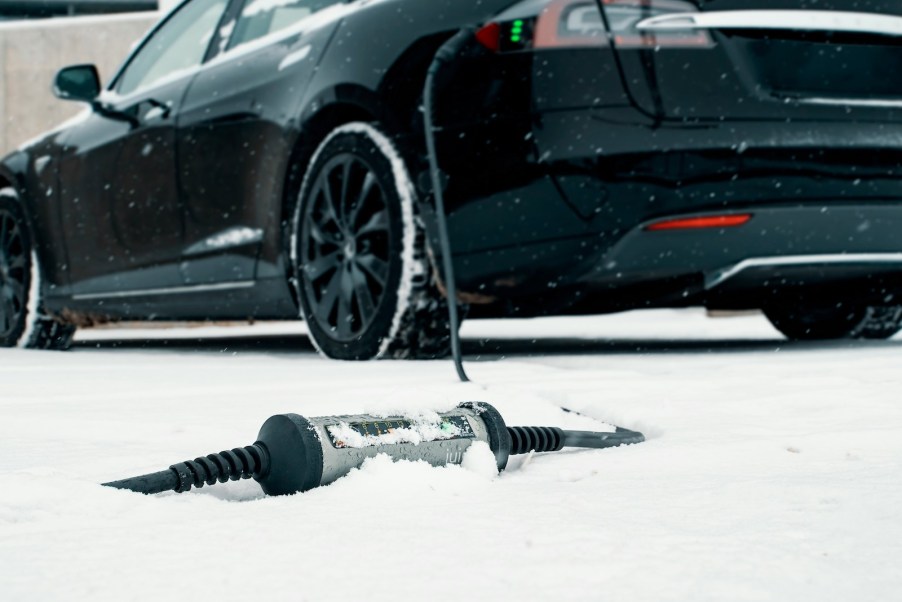 Bricked Tesla parked in the snow with its charger on the ground.