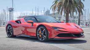 A red Ferrari SF90 Spider parked in front of a palm tree at a harbor on a sunny day