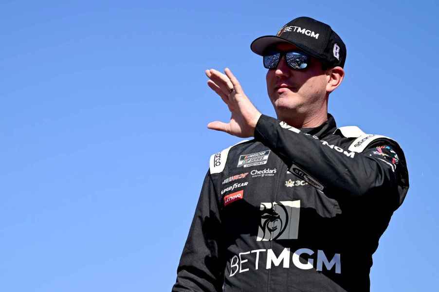 NASCAR driver Kyle Busch is showing waving with black hat and sunglasses blue sky in background