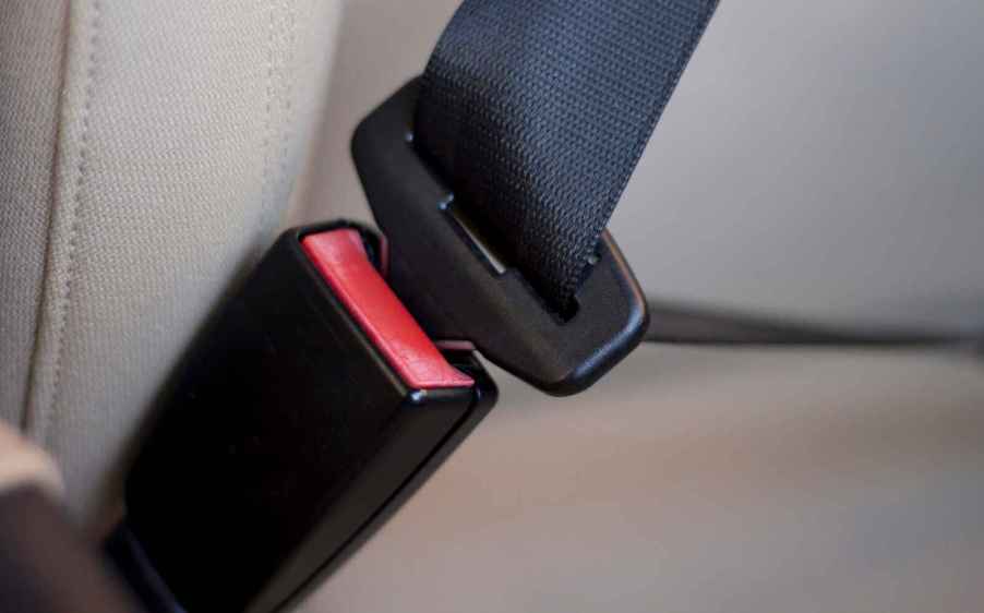 A car's black seat belt is shown buckled into the buckle without a person