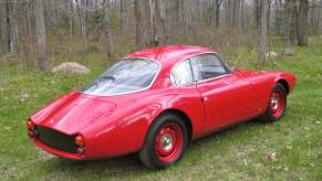 Red 1961 SSZ Stradale prototype parked in front of the woods.