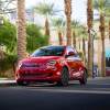 A red 2024 FIAT 500e drives past palm trees.