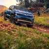 A blue 2024 Chevrolet Silverado EB drives down a grass covered dirt hill