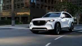 A white 2024 Mazda CX-90 PHEV SUV turning a corner on a paved downtown street