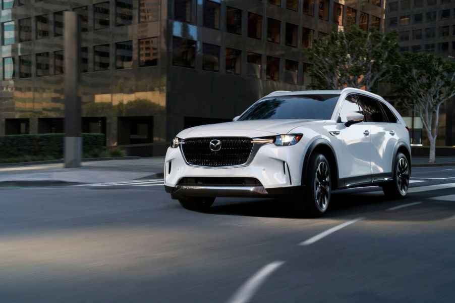 A white 2024 Mazda CX-90 PHEV SUV turning a corner on a paved downtown street