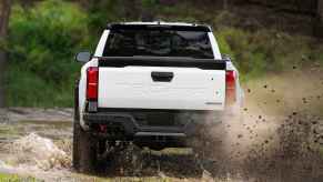 A white 2024 Toyota Tacoma truck in rear view kicking up dirt