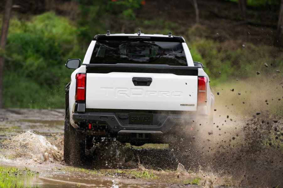 A white 2024 Toyota Tacoma truck in rear view kicking up dirt